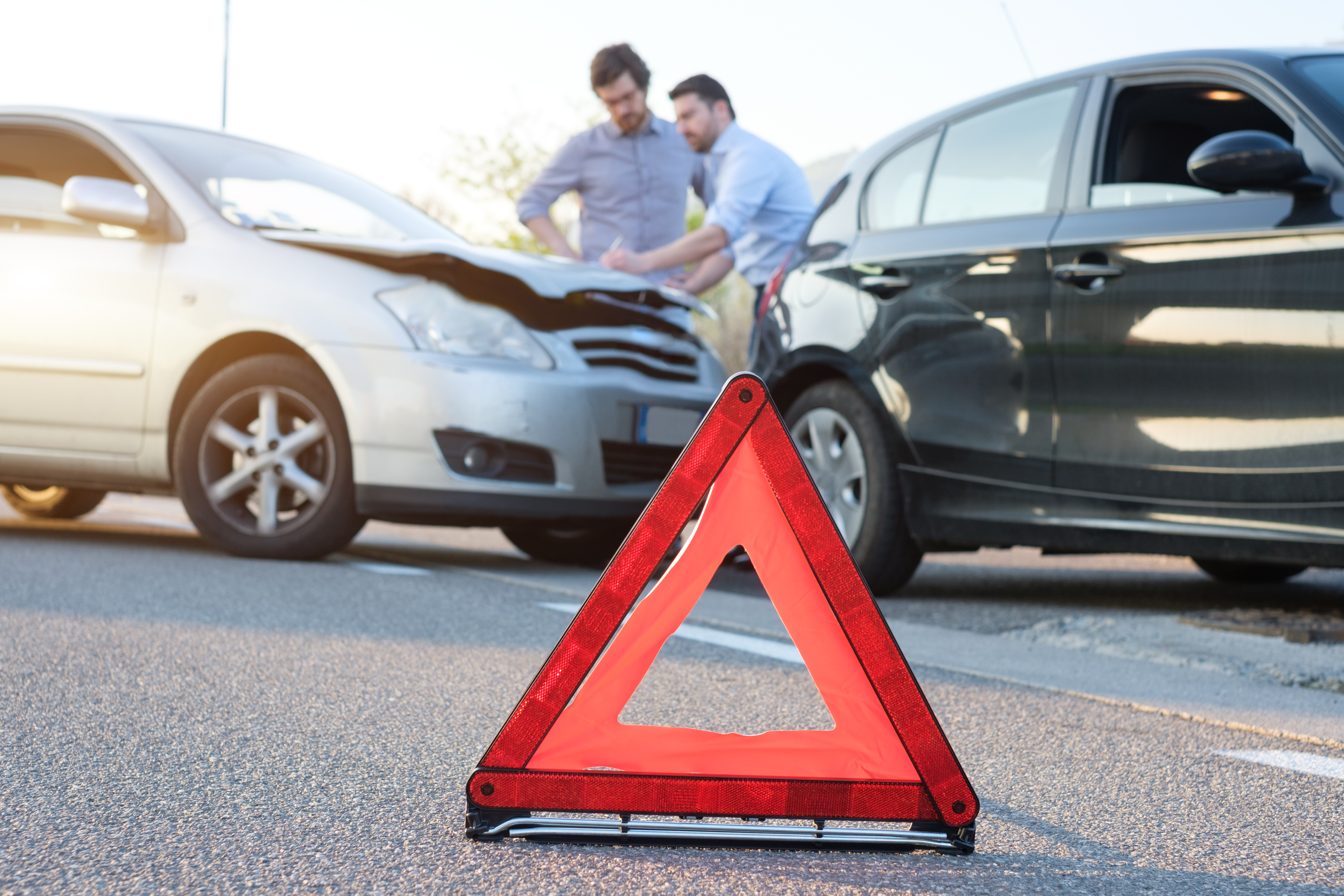 two men standing behind two vehicles that have been involved in an accident, sharing insurance information