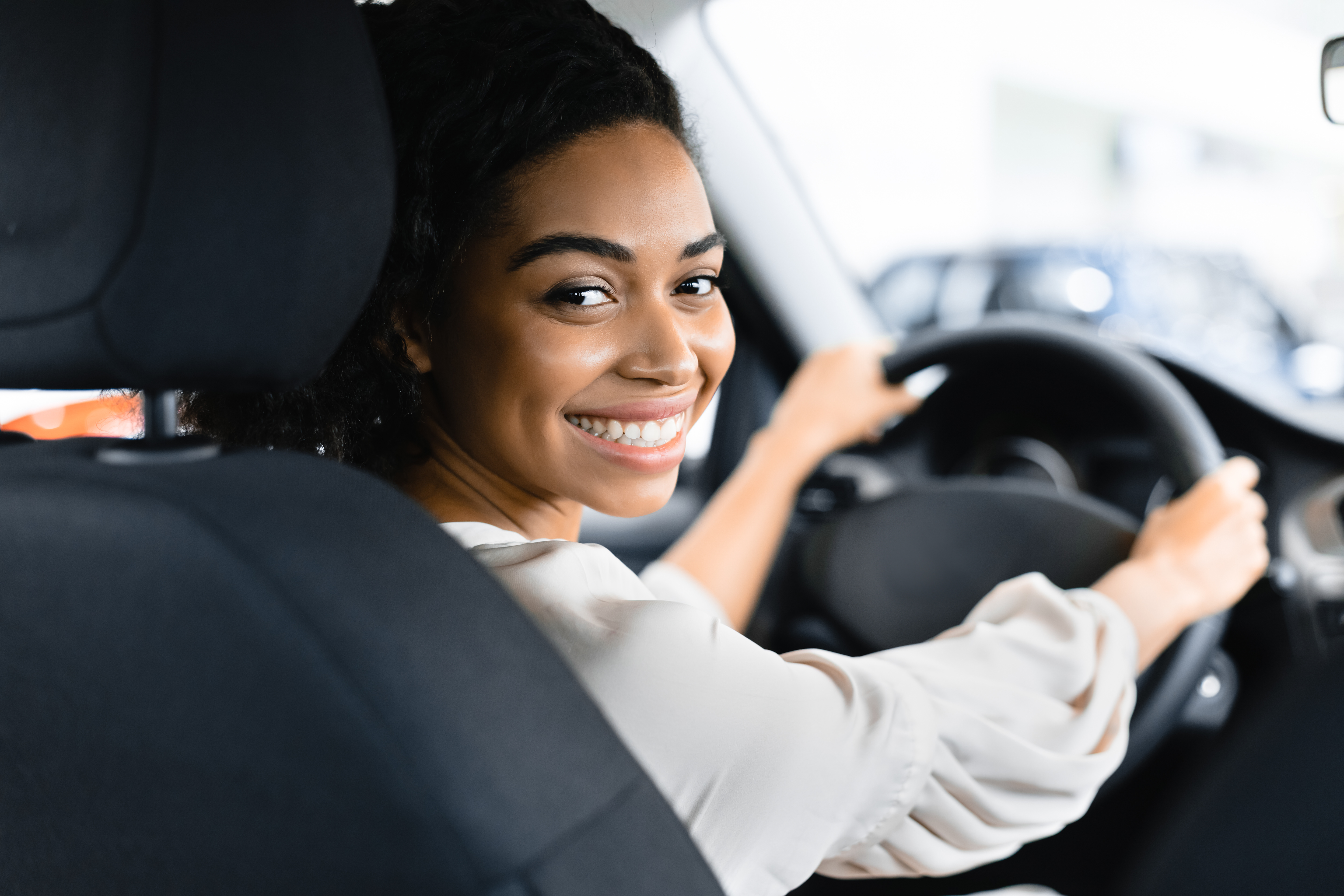 Young woman sitting in the driver seat of a car turning to face the back seat and smiling