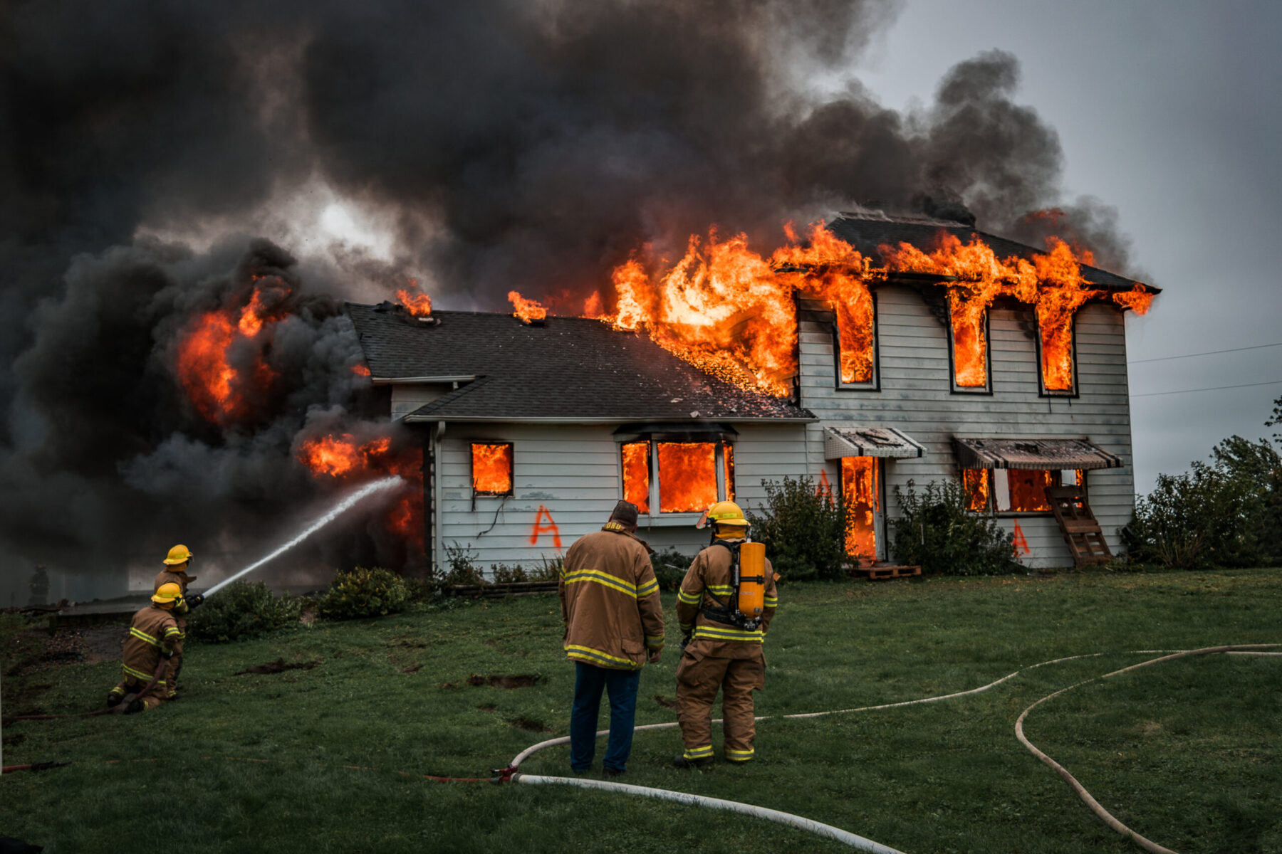 Firefighters battle a massive house fire, with flames engulfing the upper floor and thick smoke billowing into the sky.