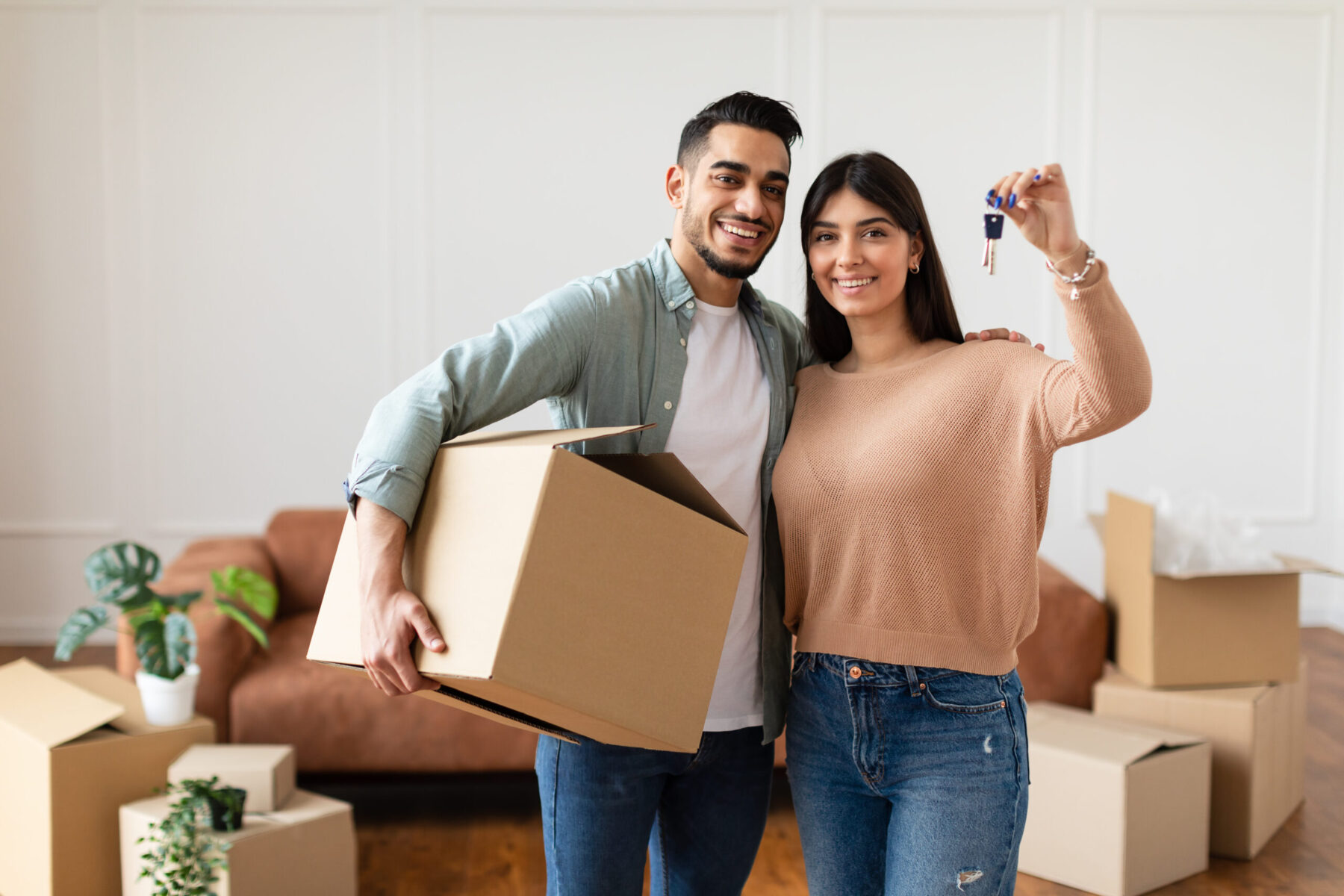 Young Couple Showing Keys And Holding Cardboard Box, Cheerful Guy And Lady Hugging After Moving In
