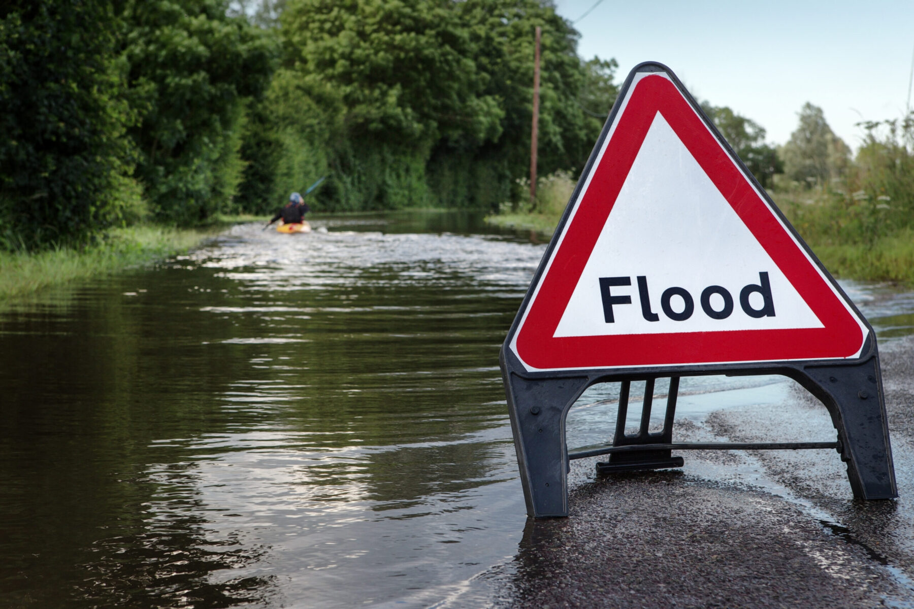 Flooded road with a person paddling down the road in a kayak.