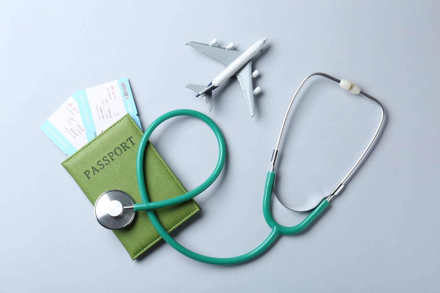Stethoscope, plane model, passport and flight tickets on light blue background.