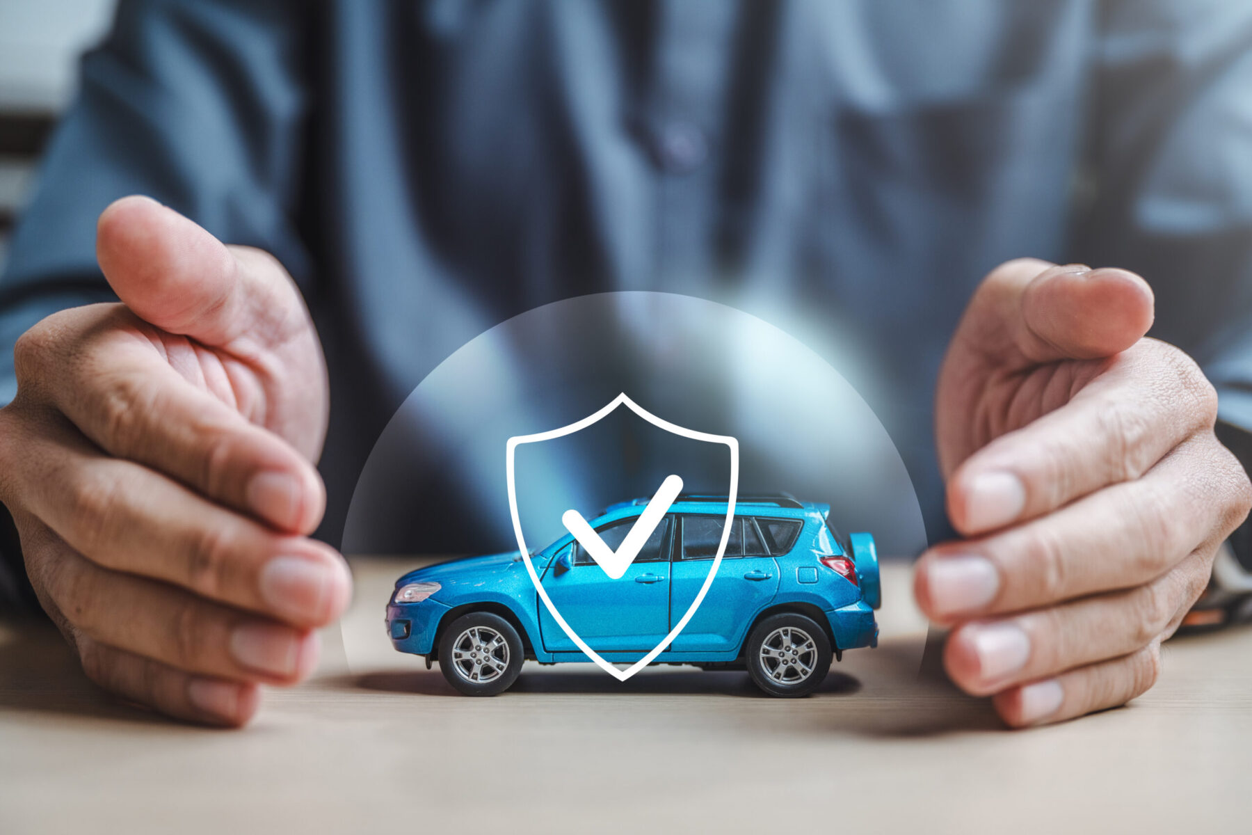 A man is holding a blue car in his hands and it has a shield on it. Concept of protection and security.