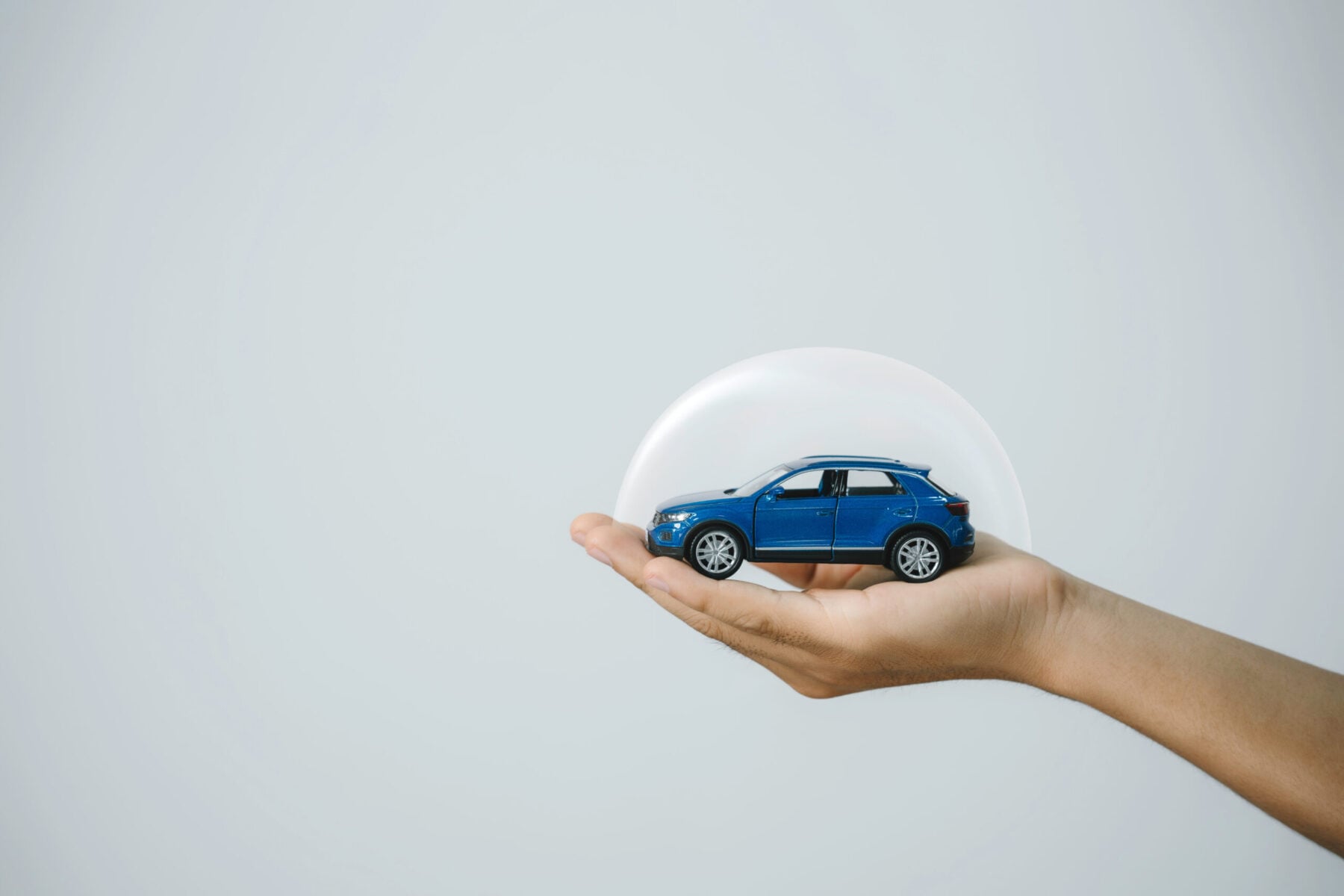 Hand-protect blue toy car under a glass dome in concept car care.
