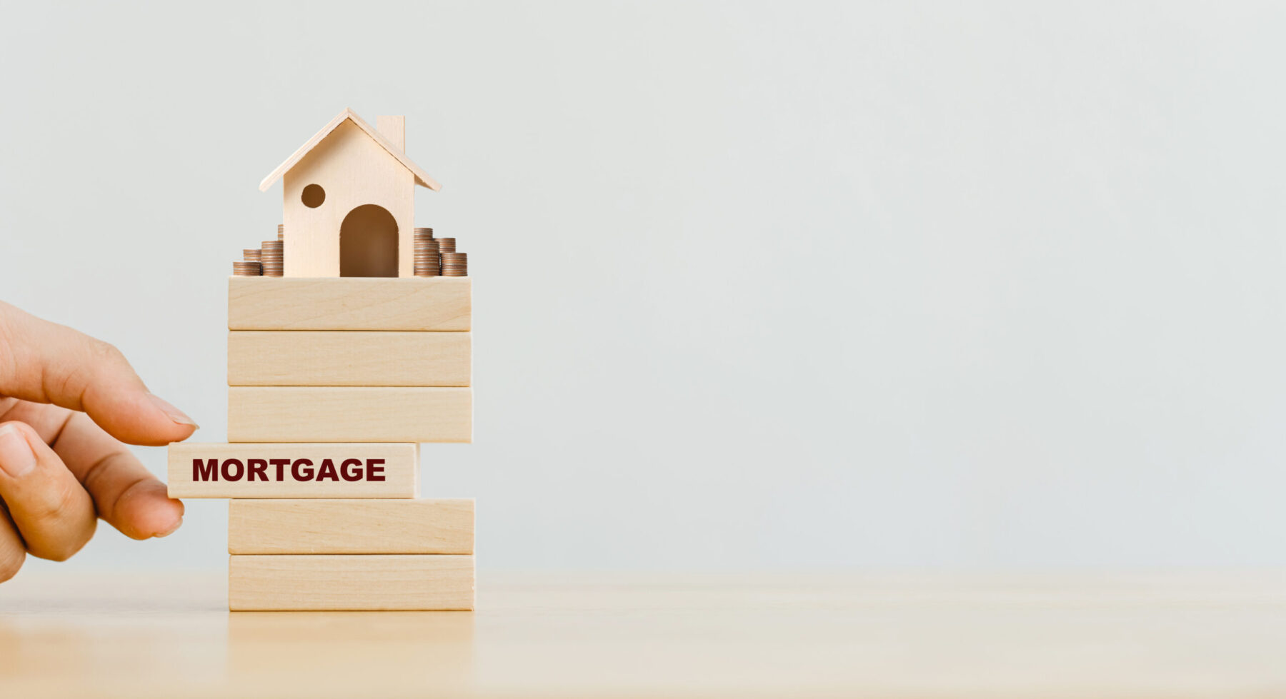 Hand putting wooden block with word mortgage and wood house with coins stack on top.
