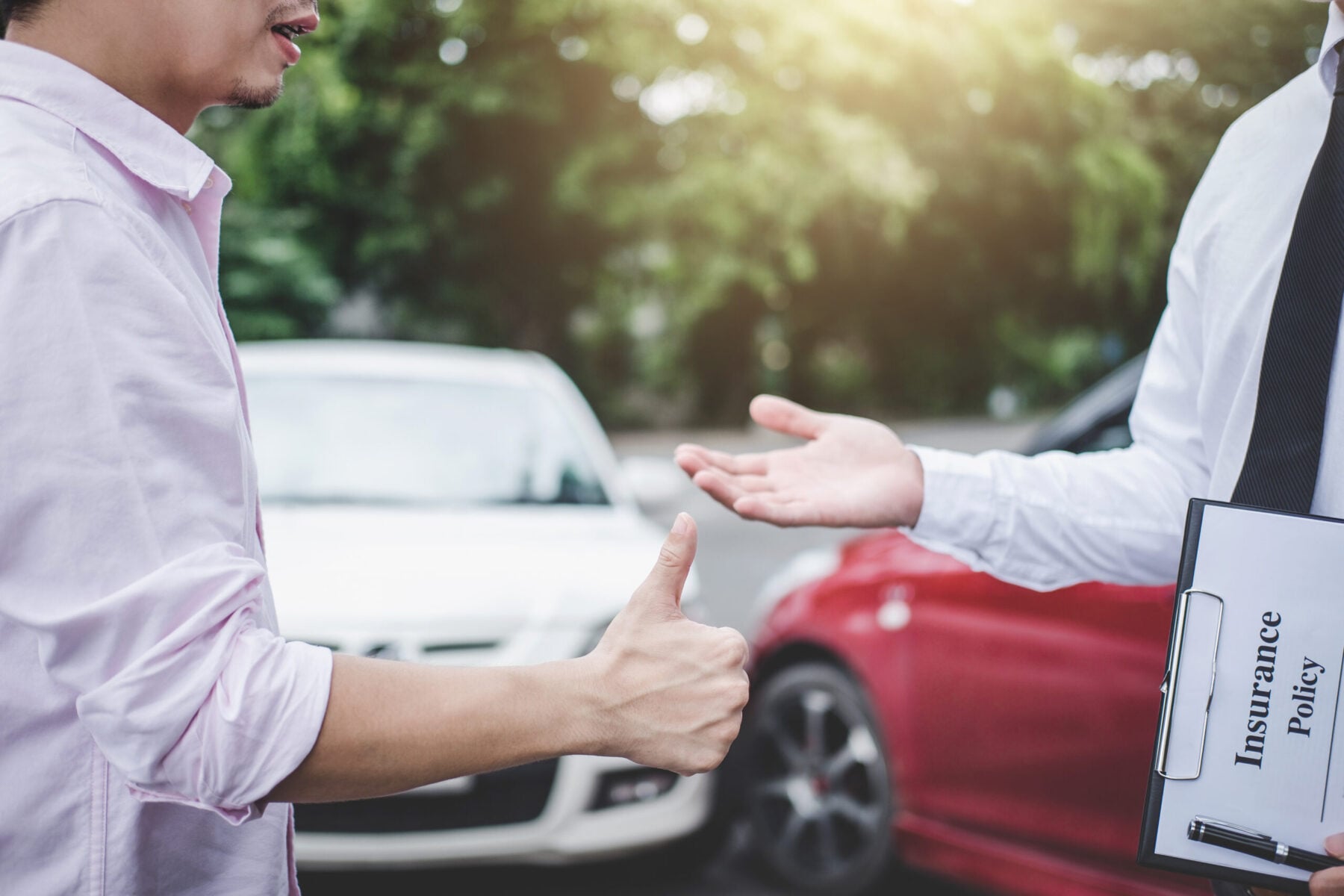 Person shaking hands with another person while holding clip board with paper with insurance policy.