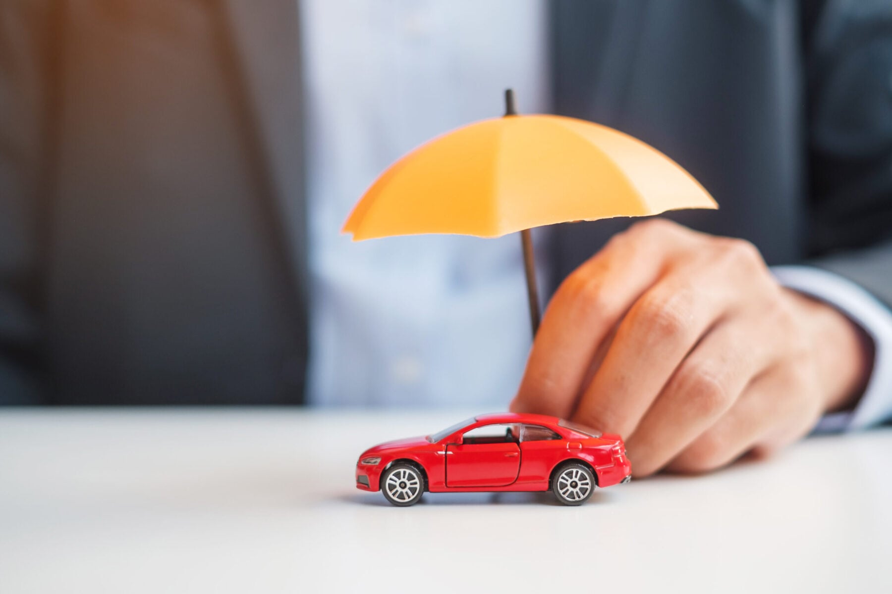 Man hand holding umbrella and cover red car toy on table.