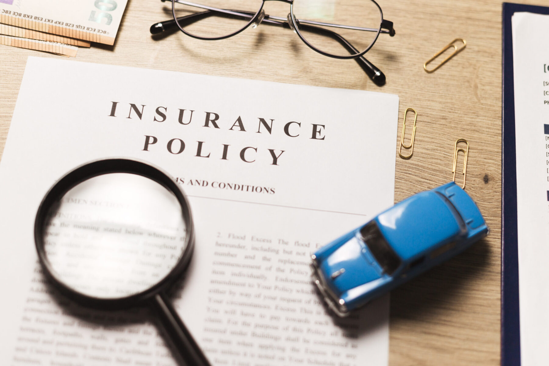 Flat lay of vehicle insurance policy. Magnifier, retro car toy and cash.