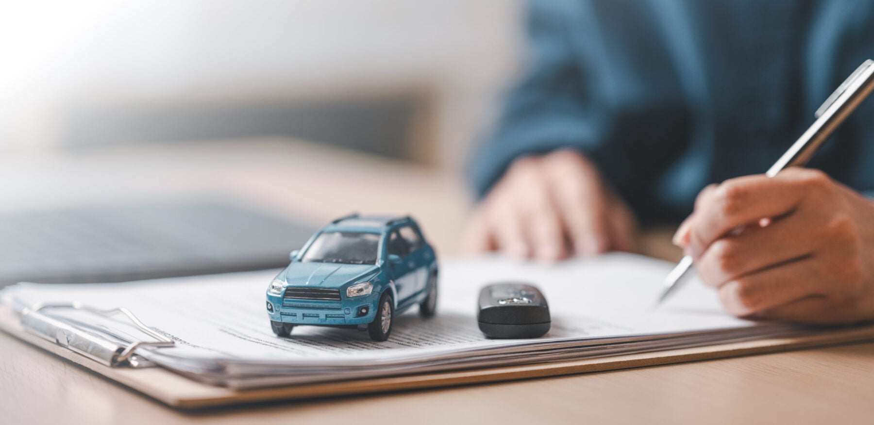 Close-up of a car model and key on a contract document with a person signing