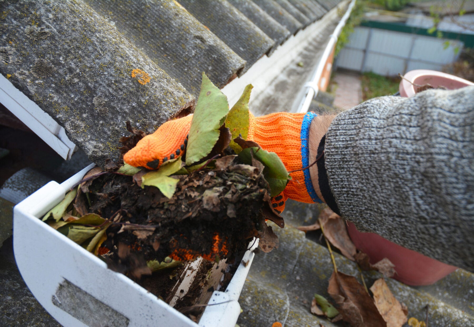 A man is cleaning a clogged roof gutter from dirt, debris and fallen leaves.