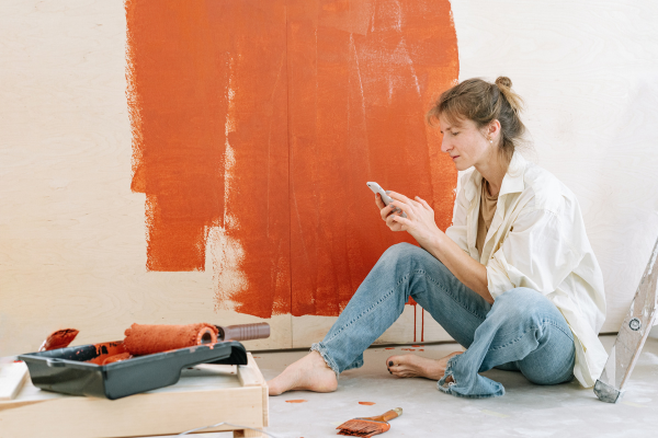 Woman sitting on floor as she rest from painting the wall orange.