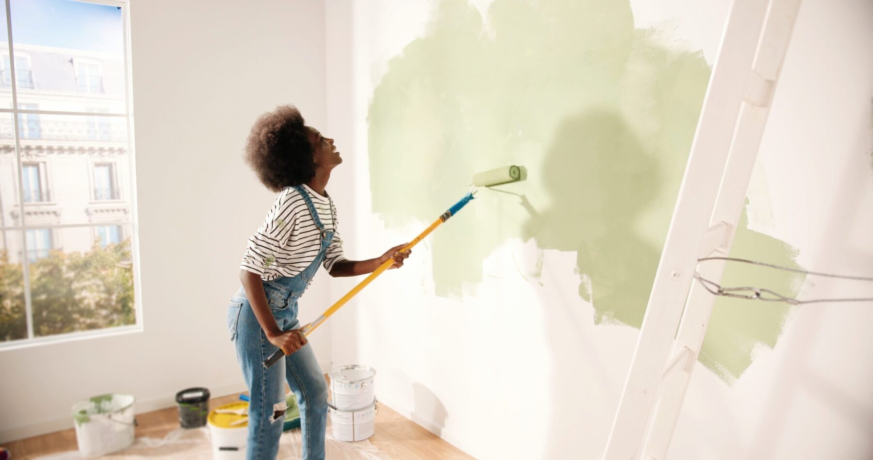 Young woman dancing and painting wall with roller brush while renovating.