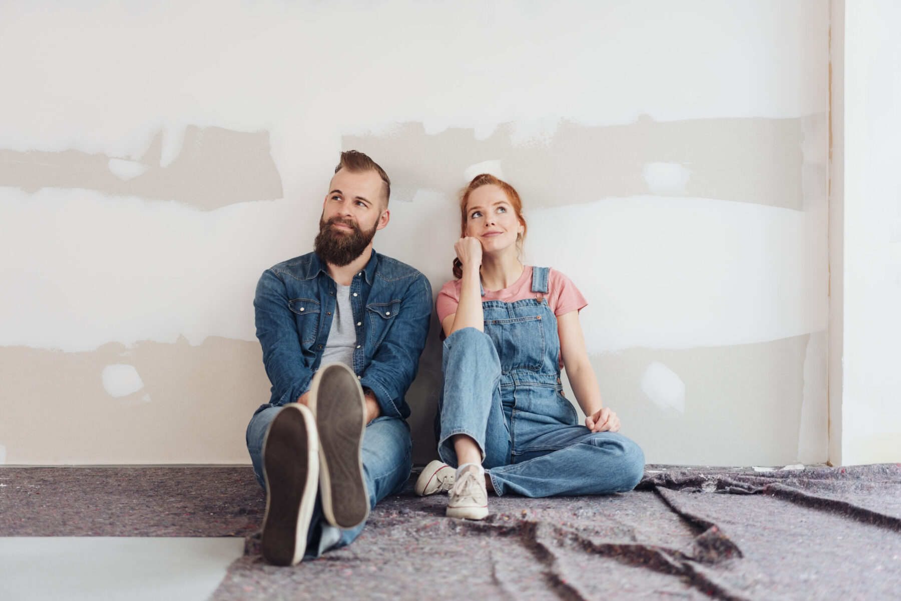 Young couple sitting on the floor side by side contemplating their handiwork.