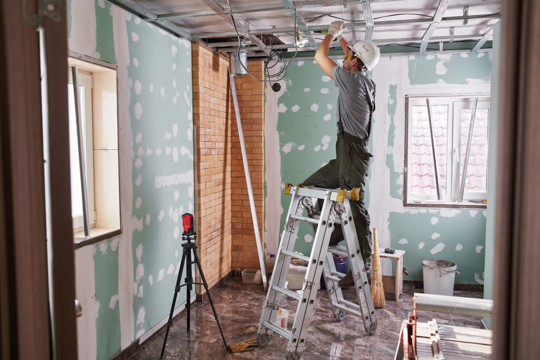 Young builder makes a plasterboard ceiling, standing on a stepladder.
