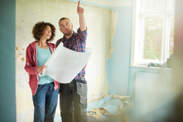 Man and woman looking at plans of house in room that is being remodeled.